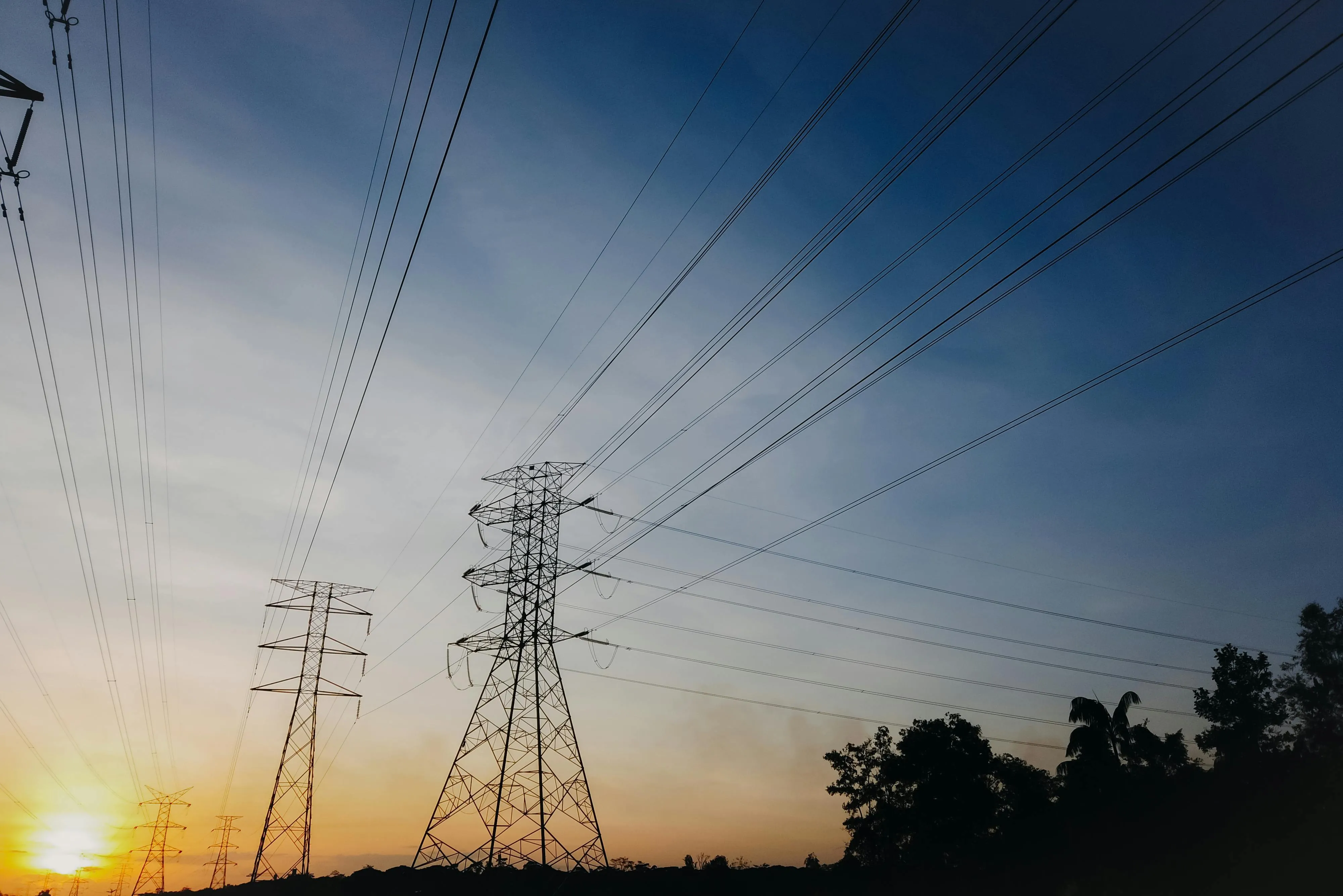 Power lines and electrical towers silhouetted against a dramatic sunset sky, symbolizing energy infrastructure and progress.
